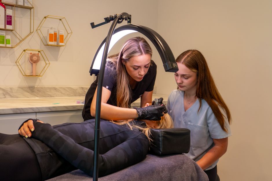 Women performing a cosmetic procedure in a modern dermatology clinic. Focus on precision and care.
